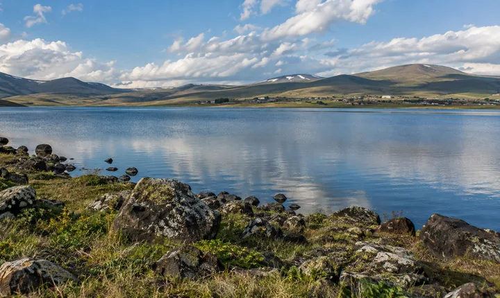 A blue highland lake bordered by grass and dark volcanic stones on Georgia's plateau