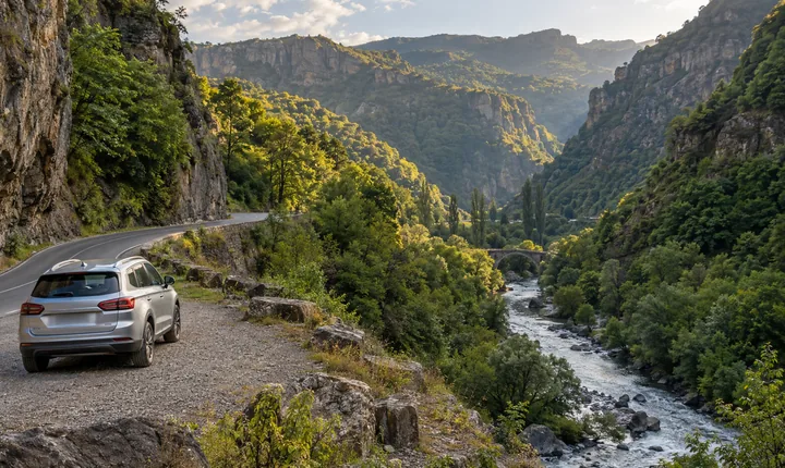 A silver SUV at a turnout beside a paved road through a forested Armenian river canyon