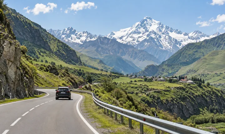 A dark SUV follows a paved winding road through Georgia's green Caucasus foothills