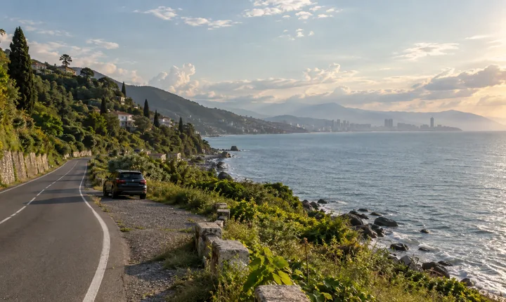 A parked SUV beside a coastal road with Georgia's Black Sea and green foothills beyond