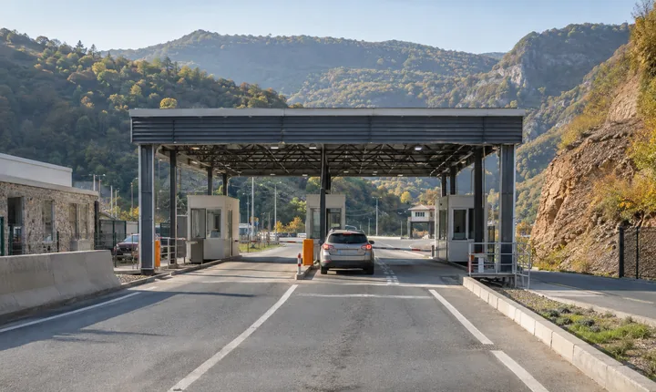 A car approaching a small vehicle border checkpoint in the wooded South Caucasus