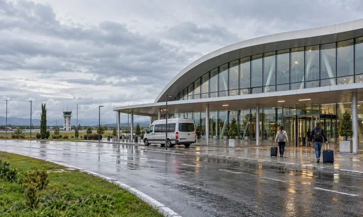A shuttle van and travelers outside a low airport terminal in western Georgia