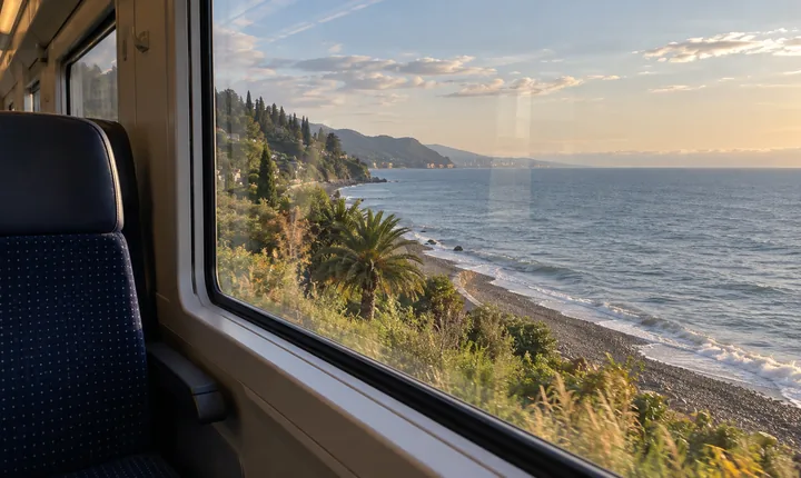 An empty train window seat overlooks the Black Sea and a pebbled Georgian shoreline