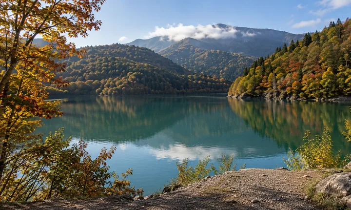 Autumn-colored forest surrounds the calm water of Shaori Lake in Racha