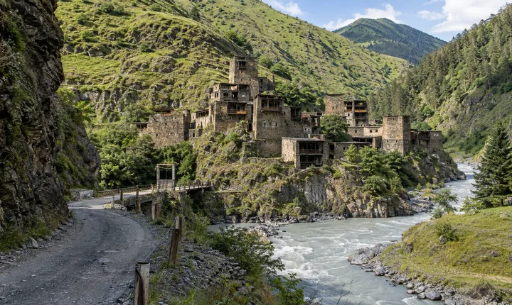Mountain road entering Shatili valley beside a river and medieval stone tower houses in Khevsureti