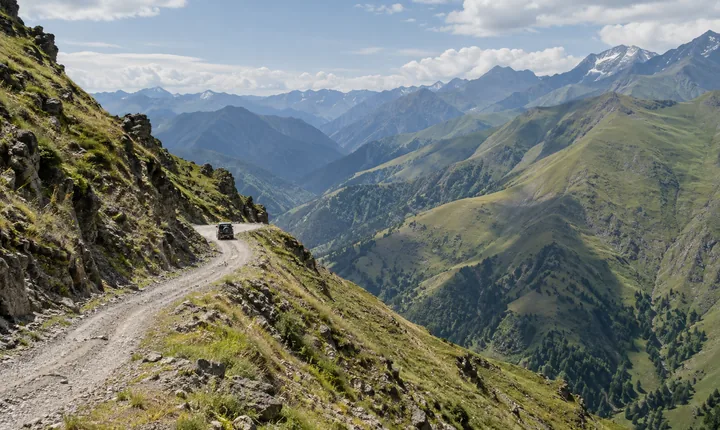 Gravel road across the Abano Pass toward Tusheti with a small 4x4 and green Caucasus slopes