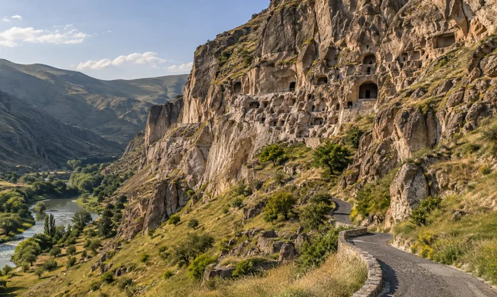 Vardzia cave monastery cut into a tan cliff above the green Mtkvari valley and its access road