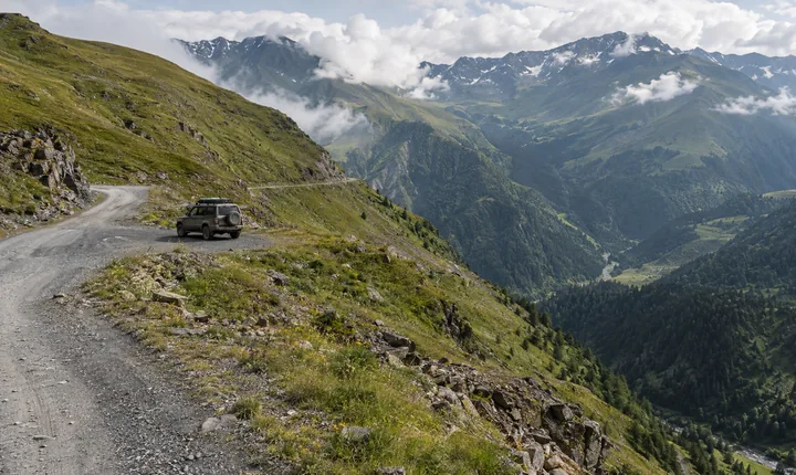 A gravel switchback winds across green slopes on Georgia's Abano Pass toward Tusheti
