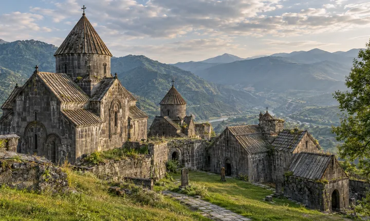 Ancient grey-stone churches with conical roofs in a grassy Armenian monastery courtyard
