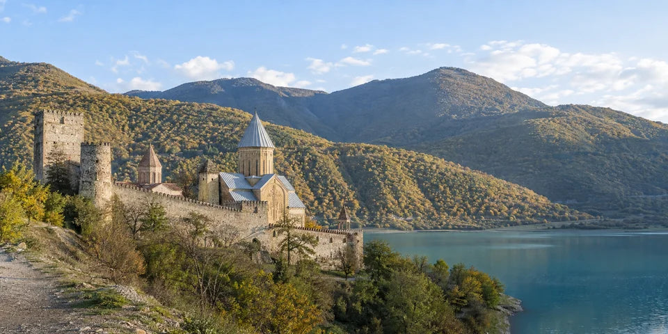 Eine steinerne Festung und eine Kuppelkirche neben einem türkisfarbenen Stausee und bewaldeten Hügeln