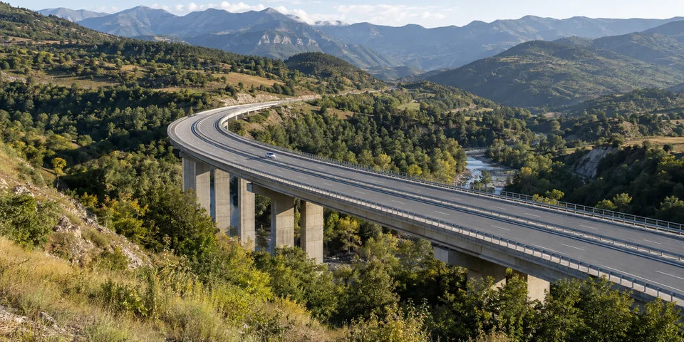 Eine Straße mit getrennten Fahrbahnen führt in einer Kurve über einen Viadukt durch Georgiens grünes Vorgebirge