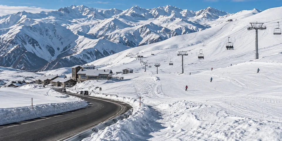 Skipisten, Sessellift und eine geräumte Zufahrtsstraße in Gudauri unter verschneiten Caucasus-Kämmen