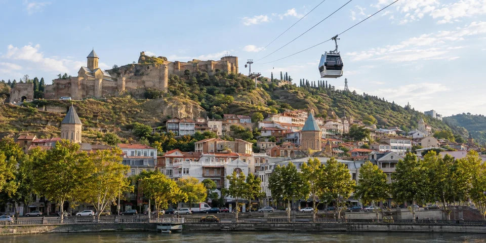 Eine Seilbahngondel fährt über den Fluss von Tbilisi, dahinter Häuser am Hang