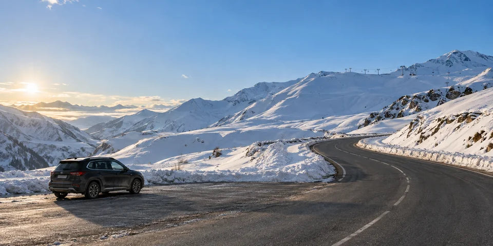 A parked SUV beside a cleared mountain road and snowy slopes near Gudauri