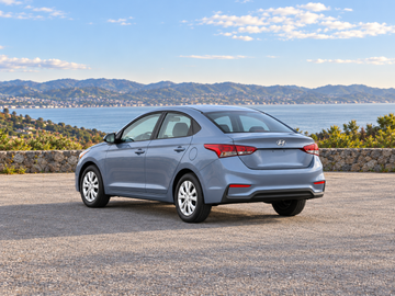 KI-generierte illustrative Darstellung: Hyundai Accent 2019, hintere Dreiviertelansicht auf trockenem Straßenbelag in landschaftlicher Umgebung. Farbe und Ausstattung des tatsächlichen Fahrzeugs können abweichen.