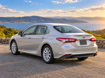 صورة توضيحية مولدة بالذكاء الاصطناعي لطراز Toyota Camry 2018, منظر خلفي بزاوية ثلاثة أرباع من جانب السائق, المقدمة باتجاه أعلى اليسار في بيئة ذات مناظر طبيعية على سطح مرصوف جاف. قد يختلف لون السيارة الفعلية وتجهيزاتها.