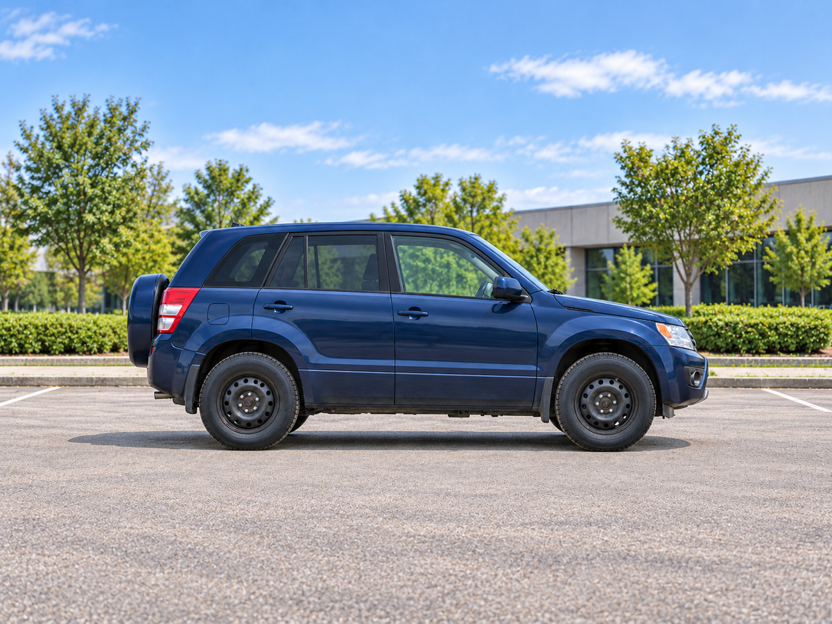 KI-generierte illustrative Darstellung: Suzuki Grand Vitara (JT, 5-door) 2013, Seitenansicht auf trockenem Straßenbelag in städtischer Umgebung. Farbe und Ausstattung des tatsächlichen Fahrzeugs können abweichen.