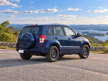 AI-generated illustrative Suzuki Grand Vitara (JT, 5-door) 2013, rear three-quarter in a dry paved scenic setting. Actual vehicle colour and equipment may vary.