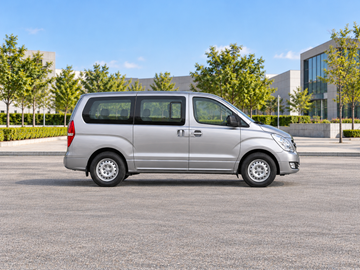 Иллюстративное изображение, созданное ИИ: Hyundai H-1 Travel 2018, вид сбоку на сухом дорожном покрытии в городской обстановке. Цвет и комплектация реального автомобиля могут отличаться.