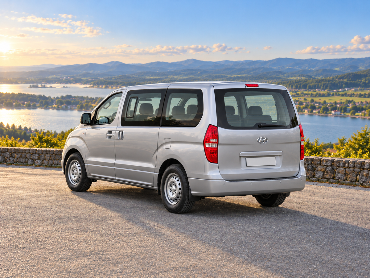 KI-generierte illustrative Darstellung: Hyundai H-1 Travel 2018, hintere Dreiviertelansicht auf trockenem Straßenbelag in landschaftlicher Umgebung. Farbe und Ausstattung des tatsächlichen Fahrzeugs können abweichen.