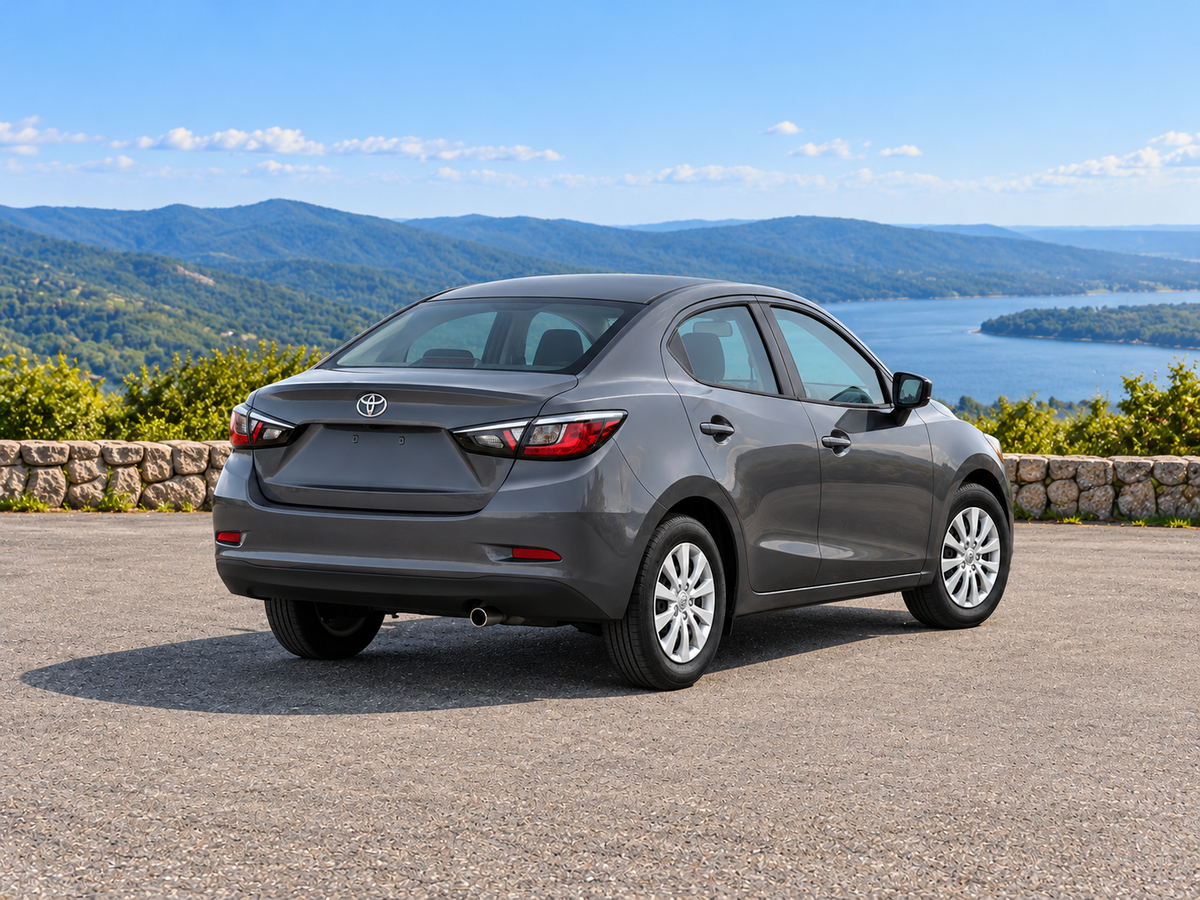 KI-generierte illustrative Darstellung: Toyota Yaris Sedan 2019, hintere Dreiviertelansicht auf trockenem Straßenbelag in landschaftlicher Umgebung. Farbe und Ausstattung des tatsächlichen Fahrzeugs können abweichen.